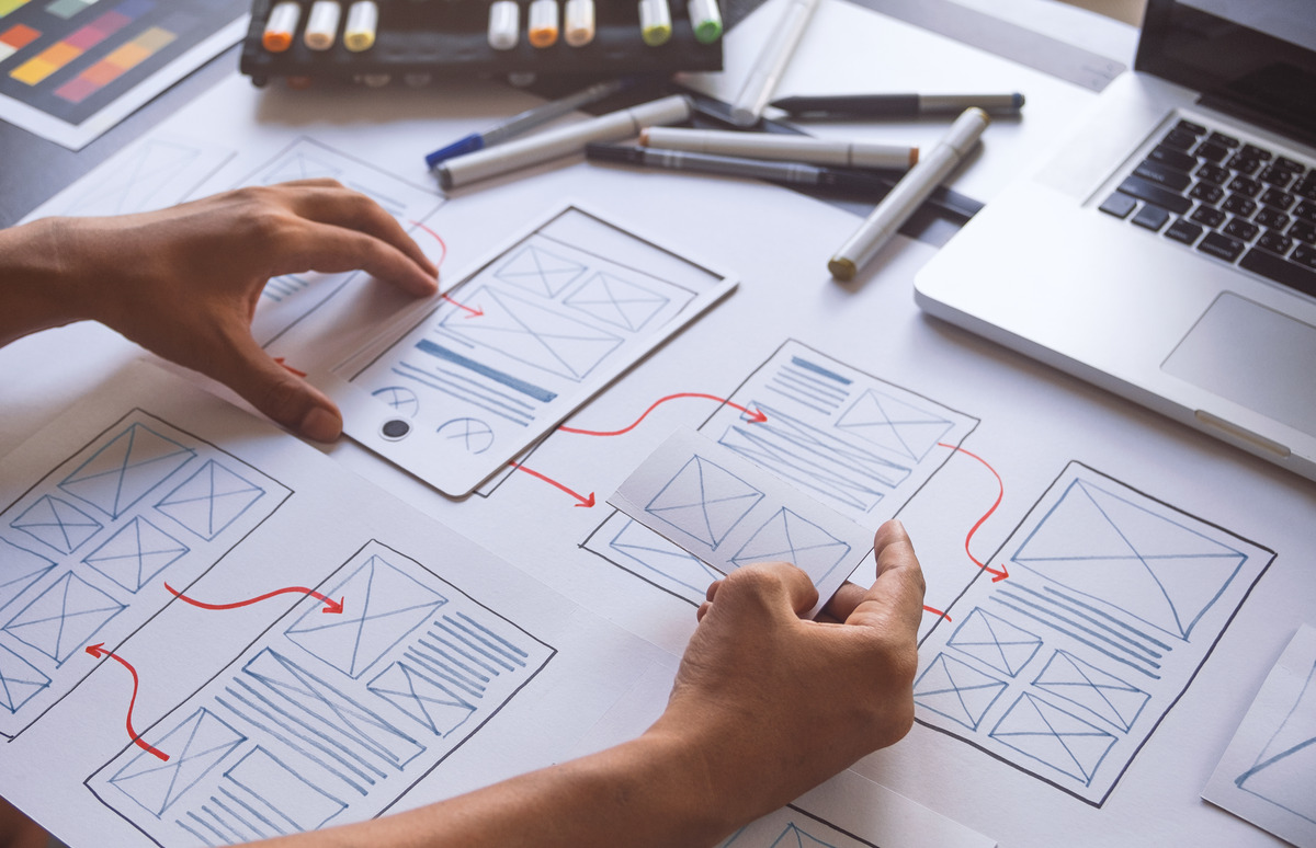 A web designer planning an Elementor website layout, with colour swatches, a graphics tablet and a page flowchart on the desk.